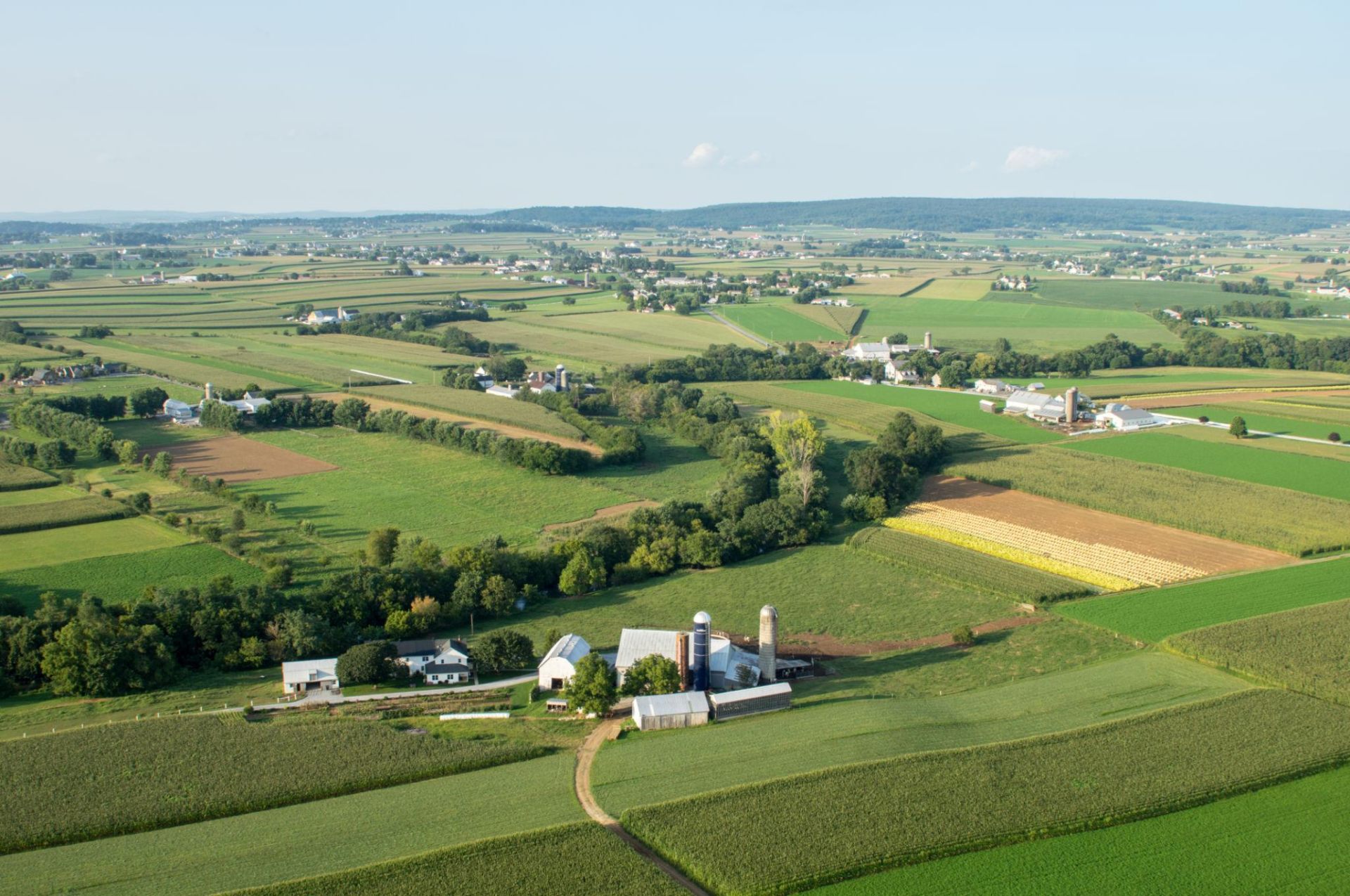 Aerial view of Lancaster County farmland with patchwork fields and a small farm at golden hour